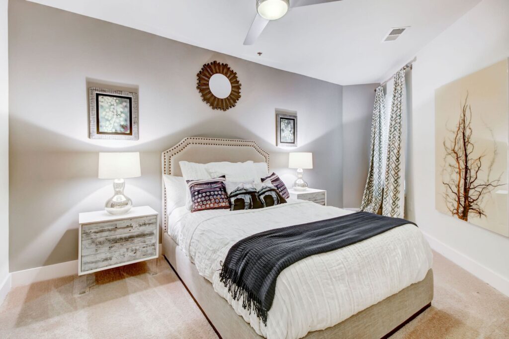 Furnished apartment bedroom with carpet flooring, a ceiling fan with light, and a window